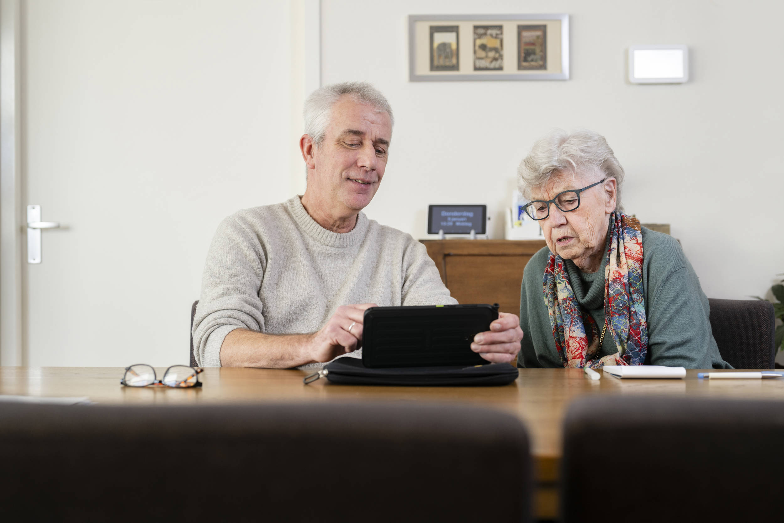 Wijkverpleegkundige praat met cliënt, laat wat zien op tablet