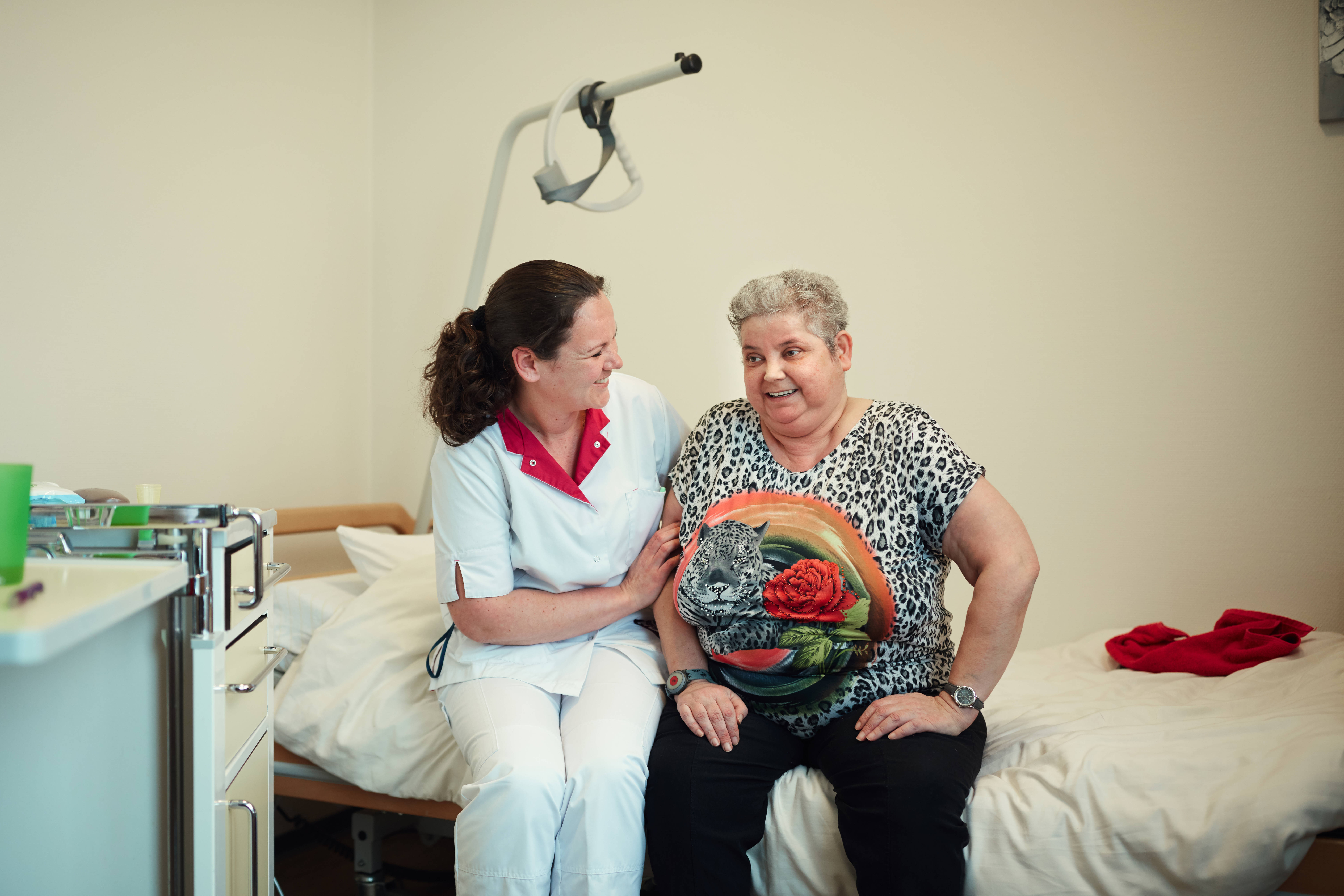 Verzorgende zit naast een cliënt op het bed