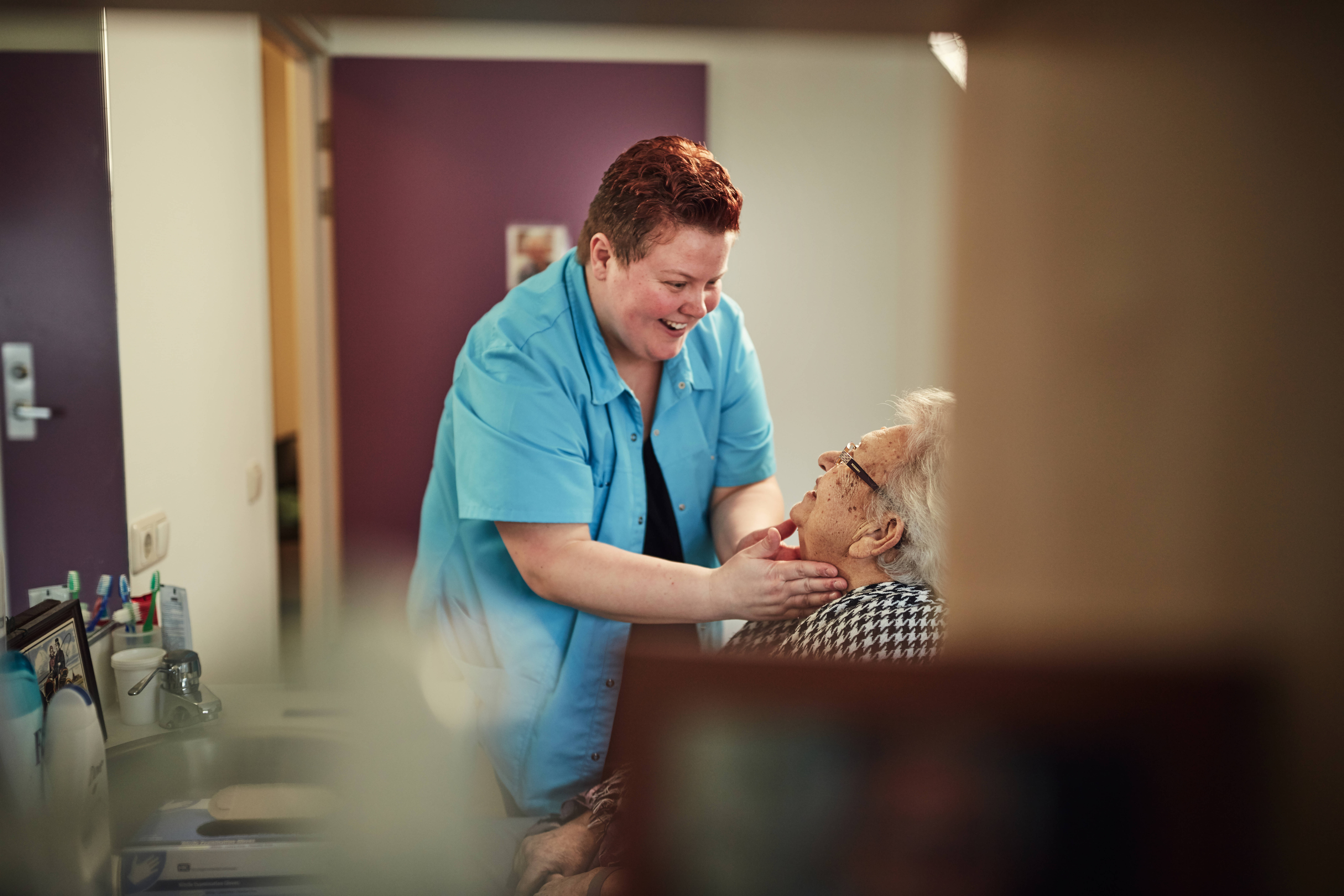 Verzorgende masseert het gezicht van oudere mevrouw in het verpleeghuis